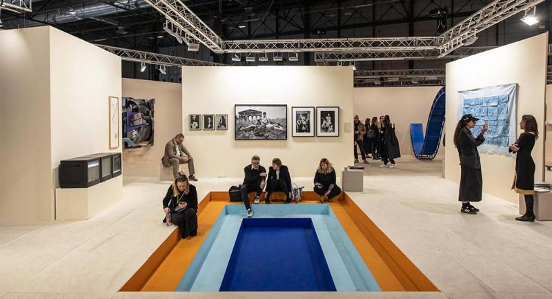 Sala de exposición de arte contemporáneo con personas sentadas en suelo de colores